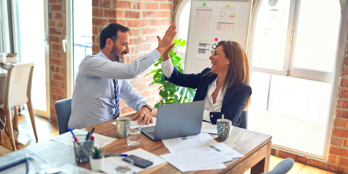 Two middle age business workers smiling happy and confident. Working together with smile on face hand giving high five at the office.