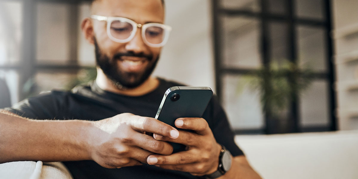 young man sits on the couch an looks at his phone, relaxed and smiling