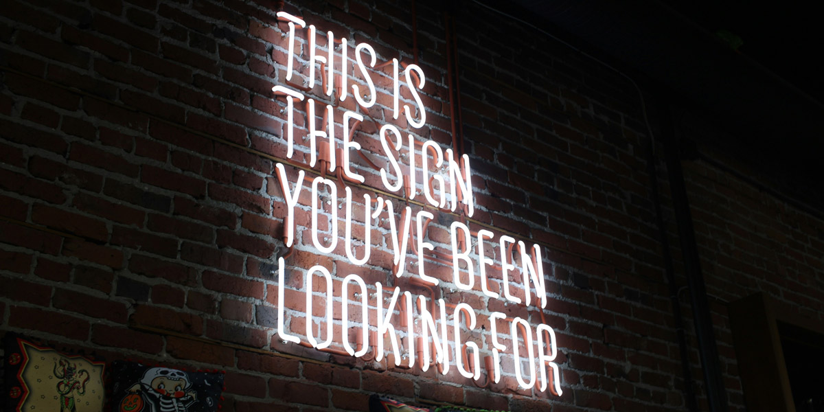 A neon sign with the text "this is the sign you've been looking for" glowing brightly in vibrant colors.