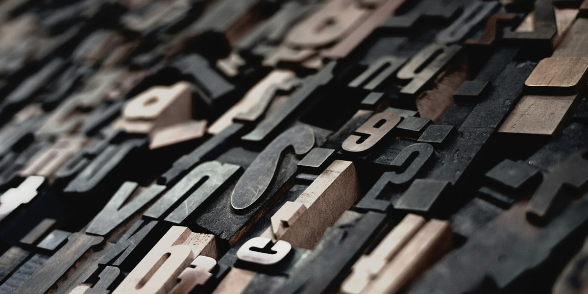 A large pile of wooden type letters arranged haphazardly, showcasing various sizes and styles in a rustic setting.