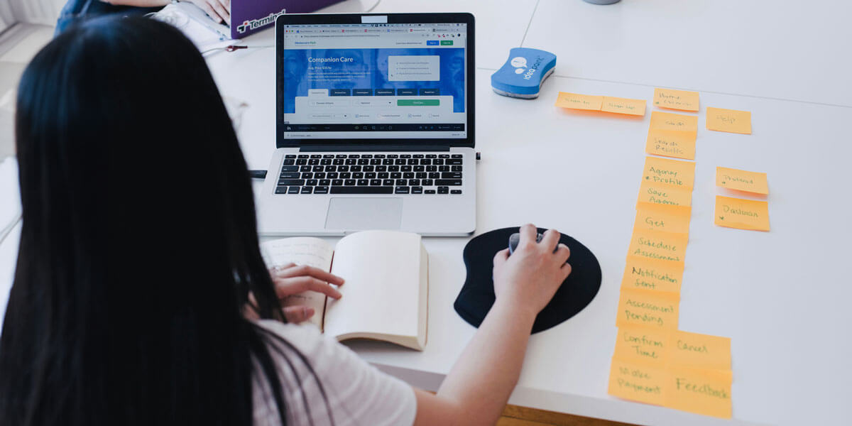 A woman works at a laptop displaying a website interface, surrounded by sticky notes and a notebook, planning a digital workflow.
