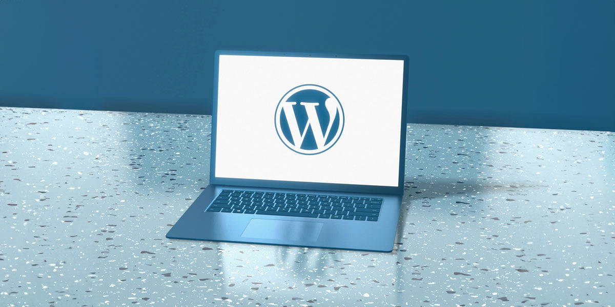 A laptop displays the WordPress logo on a clean, modern surface with a minimalistic blue background.