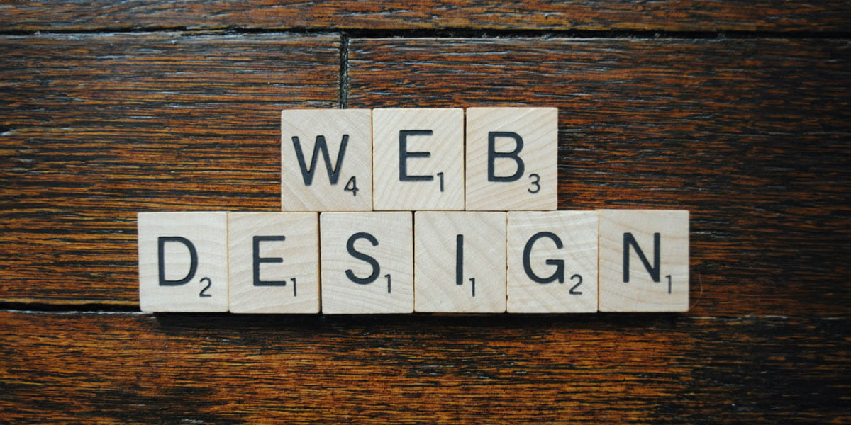 Scrabble-style wooden letter tiles spell out “Web Design” on a dark wooden surface, suggesting creativity and craftsmanship.