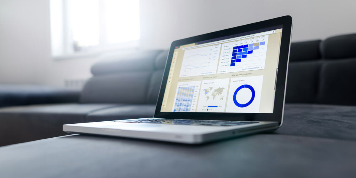 A laptop on a couch displays multiple analytics dashboards and charts, including graphs, heatmaps, and circular diagrams.