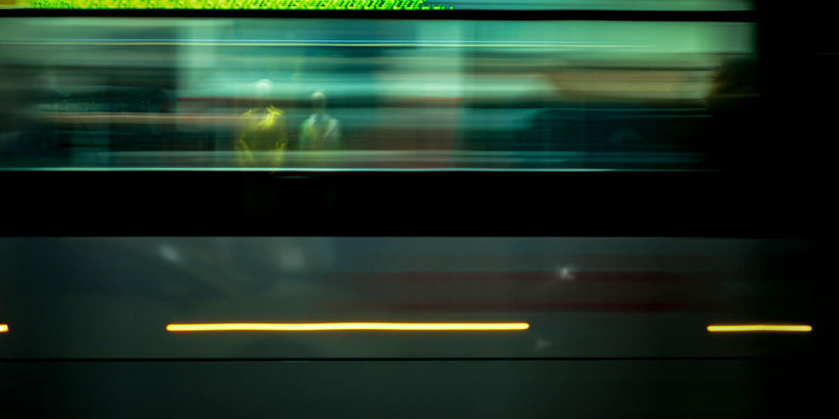 Blurred motion photo of a subway train passing by with faint reflections of people visible inside.