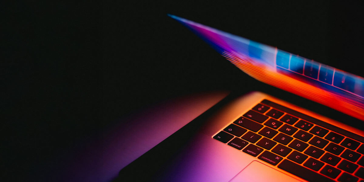 Partially open laptop glowing with vibrant neon colors against a dark background.