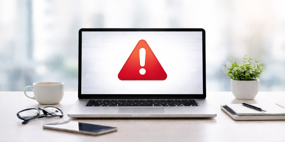 A laptop displays a warning symbol on the screen, representing a website issue or system alert that requires immediate attention.