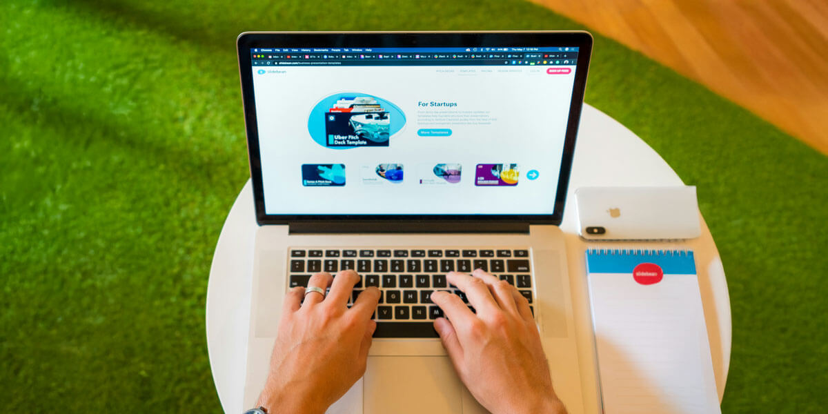 Hands typing on a laptop at a desk with a phone and notepad nearby, working on a website layout.