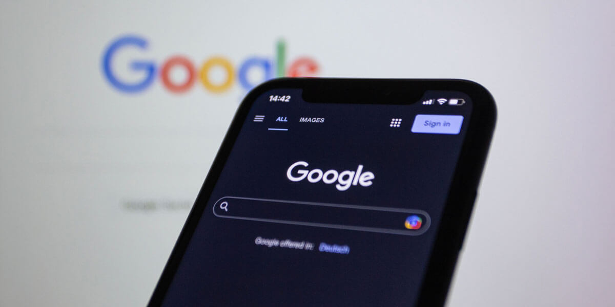 Close up of a smartphone showing the Google search homepage in front of a blurred Google logo.
