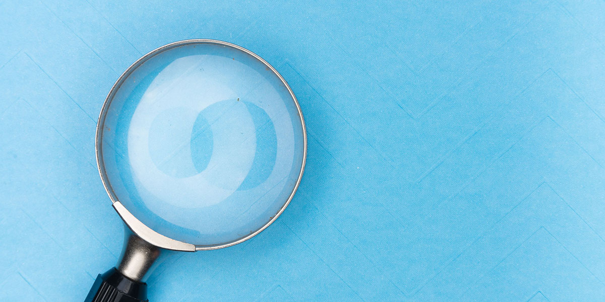A magnifying glass rests on a plain blue background with copy space to the right.